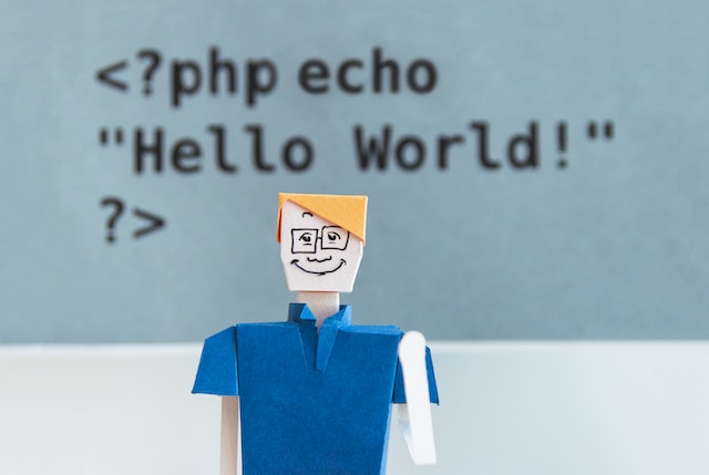 A paper toy in front of a computer screen showing a php echo statement.