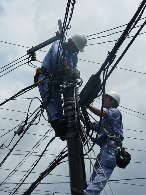 Two electricians atop an electrical pole checking the wiring