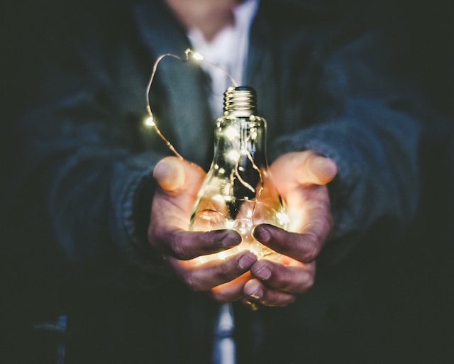 A person holding a lighted bulb in his hands