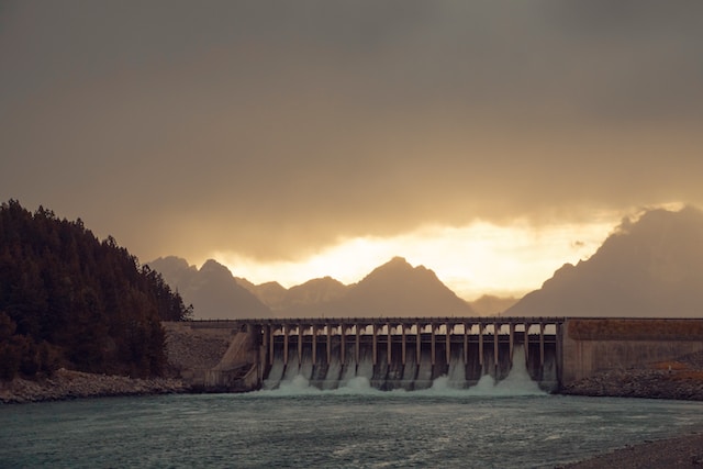 A water dam with the gray skies and the fading light of the sun behind it