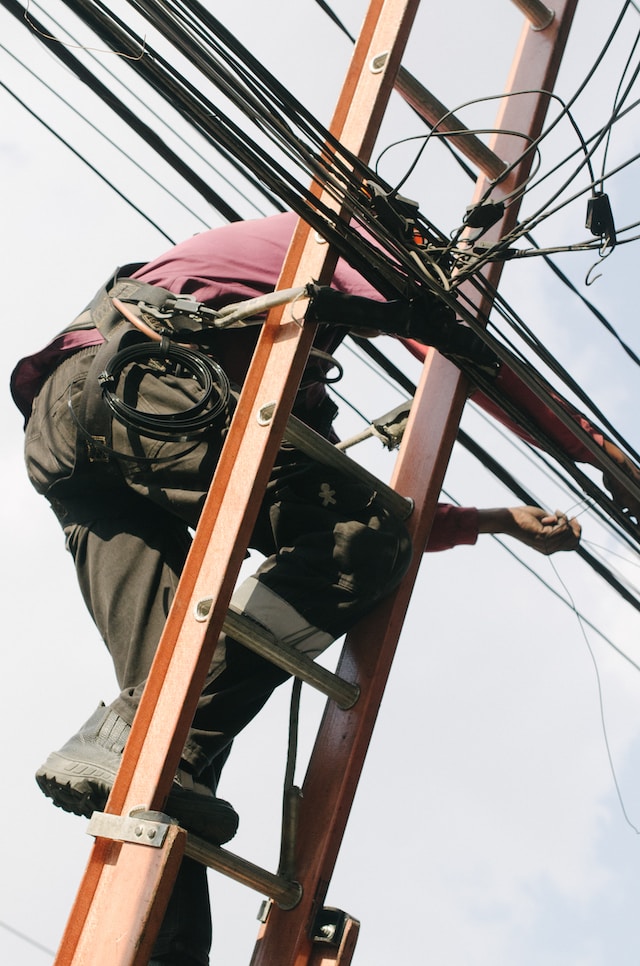 An electrician on a ladder working on electrical lines