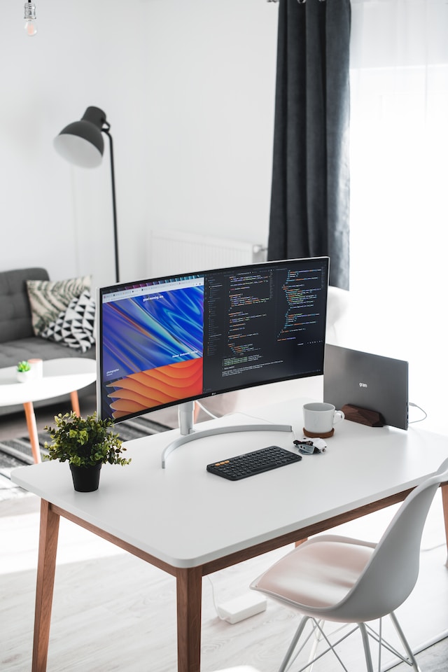 Curved monitor with code on screen on top of a white wooden desk