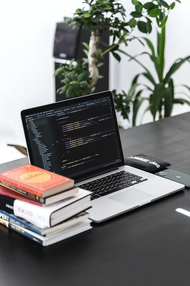 Open laptop beside a stack of books showing computer codes on the screen 